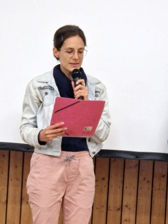 Eine Frau liest die Ehrung zum Nachhaltigkeitspreis auf der Bühne, vor einer Leinwand vor.