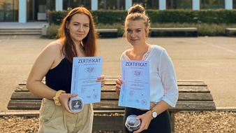 Zwei Schülerinnen auf dem Pausenhof mit jeweils einem Zertifikat in der Hand