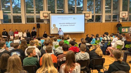Schuljahresanfangsfeier in der Turnhalle, Schülerinnen hören einem Lehrer aufmerksam zu