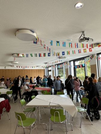 In der Mensa der HHRS sind Tische in Gruppen zusammengestellt und Menschen sitzen und stehen in Gruppen beisammen