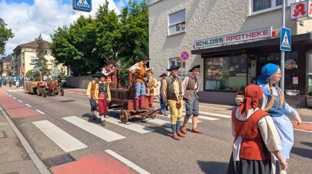 Frauen verkleidet als Waschfrauen laufen auf einer Straße in Göppingen. Dahinter altmodisch verkleidete Herren, die einen Wagen ziehen