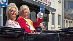 eine Frau und ein Mann altmodisch verkleidet in einem Wagen lächeln
