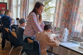Eine Frau, die einem Jungen zeigt wie man näht