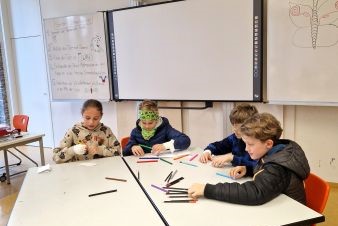 Mehrere Personen die an einem Tisch sitzen, auf dem Tisch befinden sich mehrere Stifte