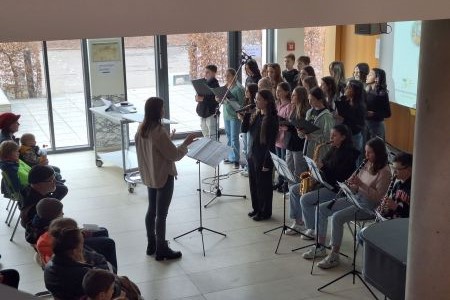 Eine Dirigentin und ein Chor, rechts daneben 3 Personen, die Saxofon und Klarinette spielen